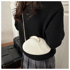 Detail of egg-shaped acrylic evening bag with gold chain strap on a model