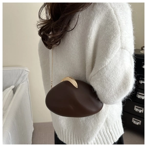 Model wearing dark brown pebble-shaped acrylic evening bag with gold chain strap
