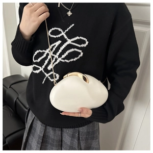 Detail of white egg-shaped acrylic bag with sleek gold clasp and chain strap on a black sweater