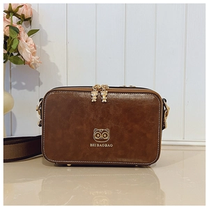 Detail showing the retro brown leather camera bag with golden zippers and cat logo