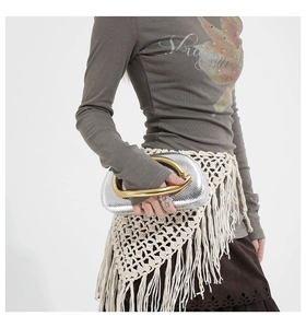 Detail of silver metallic wrist bag with a bold gold circular ring handle and fine texture