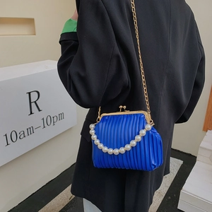 Blue pleated shell bag with pearl handle and gold chain strap worn over a black blazer