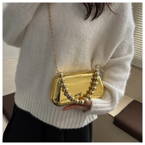 Détail du sac coquille doré miroir avec poignée perlée et chaîne sur un mannequin