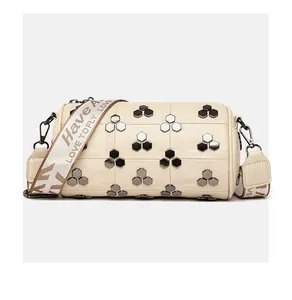 Détail macro du cuir grainé blanc crème et des rivets hexagonaux argentés sur le sac