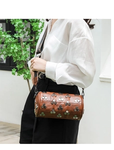 Détail d'un sac cylindre en cuir marron avec rivets hexagonaux et bandoulière tissée