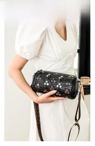 Détail du sac cylindrique noir à rivets avec bandoulière à motifs sur un mannequin