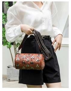 Gros plan du sac cylindre marron avec clous hexagonaux et bandoulière imprimée