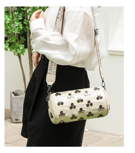 Gros plan du sac seau cylindrique crème avec rivets hexagonaux et bandoulière large tissée
