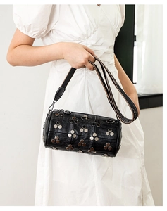 Vue détaillée du sac cylindrique noir avec rivets métalliques et bandoulière tissée