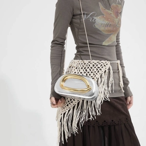 Silver metallic chain bag with a large gold curved handle, worn by a model in a studio