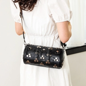 Sac à bandoulière cylindrique en cuir noir avec rivets argentés sur une robe blanche