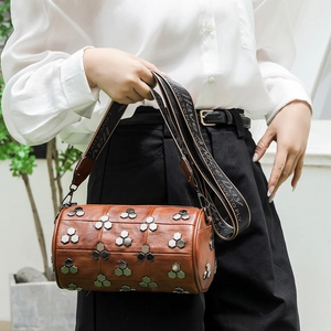 Sac cylindrique marron à rivets avec large bandoulière porté par un mannequin urbain