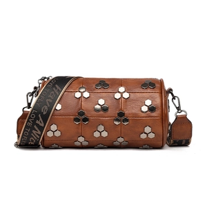 Sac cylindre marron à rivets avec large bandoulière à lettres sur fond blanc