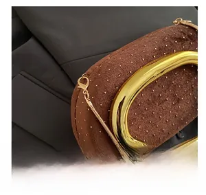 Detail of gold metal oval handle and rivet hardware on brown velvet evening clutch