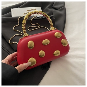 Detail van rode lederen box-tas met gouden kralen handvat en slangenketting op zwart pak