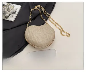 Close-up of champagne gold heart chain bag showing its mini size relative to a smartphone