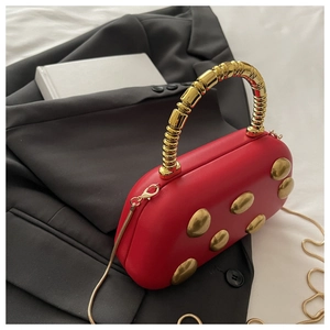 Detail van rode capsule tas met gouden kralenhandvat en studs op een grijs pak