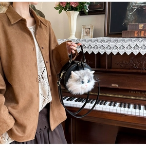 Detail shot of a black round crossbody bag with a realistic furry cat head and blue eyes