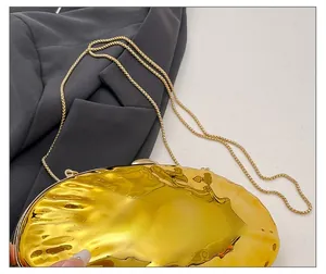Dettaglio borsa da sera dorata con trama a conchiglia e sottile tracolla a catena