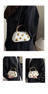 Detail van witte box clutch met gouden hardware en spiraalvormig handvat op zwarte jas