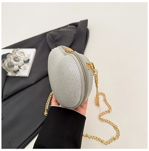 Detail of silver glitter heart bag with gold chain strap held against a grey blazer