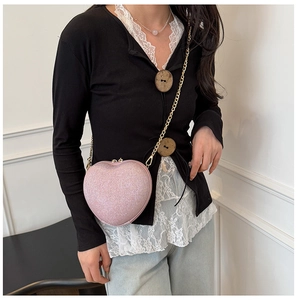 Pink glitter heart-shaped bag with gold chain strap worn by a model in a fashion setting