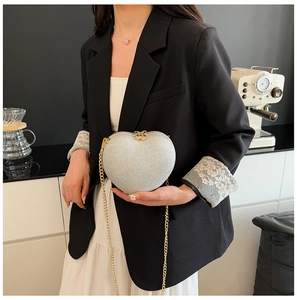 Close-up of heart-shaped silver glitter evening bag with gold chain strap shown by model