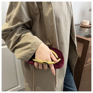Detail of burgundy velvet evening bag featuring a distinctive gold circular metal handle