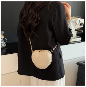 Detail of champagne glitter heart-shaped bag with gold chain strap on a black blazer