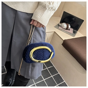 Detail of dark blue velvet clutch with gold metal clasp and chain held by model