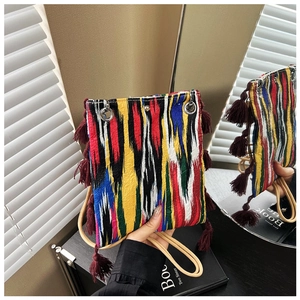 Détail d'un sac bandoulière ethnique tissé avec rayures colorées et pompons rouges