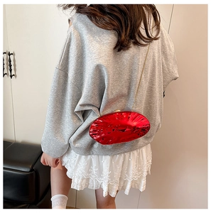 Dettaglio di una borsa da sera rossa metallizzata con catena dorata su una gonna bianca