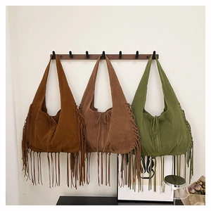 Three bohemian suede tassel tote bags in brown, beige, and olive green on a rack