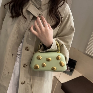 Pistachegroene boxtas met gouden klinknagels en spiraalhandvat gedragen met beige trenchcoat