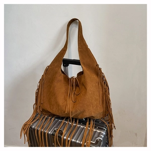 Detailed close-up of brown fringe hobo bag with suede texture on a silver suitcase