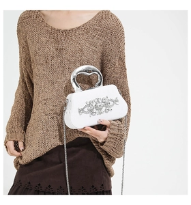Detailed view of luxury white clutch bag with floral rhinestone inlay and silver handle
