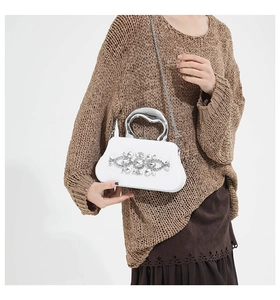 Detail view of white evening bag with crystal flower cluster and silver sculptural handle