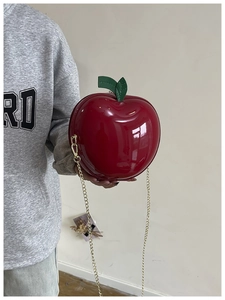 Sac pomme rouge brillant avec feuille verte et chaîne dorée porté par un mannequin