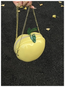 Détail macro du sac pomme en cuir verni jaune avec fermeture éclair en feuille verte
