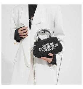 Detail of a black glitter evening bag featuring a rhinestone flower pattern and silver handle