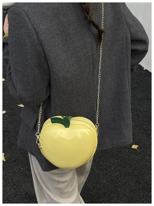 Détail d'un sac jaune en forme de pomme avec bandoulière dorée porté par un modèle