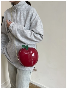 Détail du sac pomme rouge avec chaîne dorée porté sur un sweat à capuche gris
