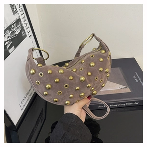Détail du sac croissant en daim fauve avec clous dorés et poignée anneau, posé avec livres
