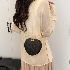 Fashionable heart-shaped crossbody bag in black glitter with gold chain strap worn by model