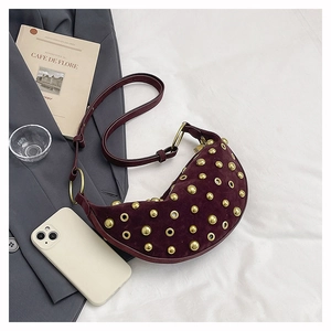 Détail d'un sac demi-lune en daim bordeaux avec clous dorés et œillets métalliques