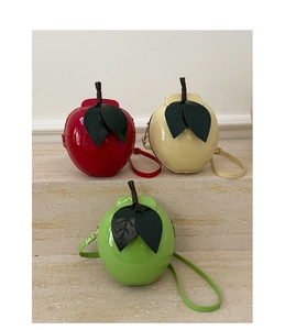 Three apple-shaped crossbody bags in red, yellow, and green patent leather on stone steps