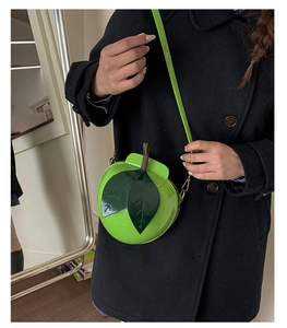 Creative bright green apple shaped crossbody bag with leaf detail on a black coat