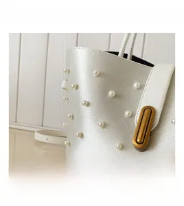 Dettaglio di eleganti decorazioni in perla e chiusura dorata sulla borsa a tracolla bianca