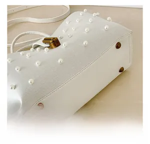 Dettaglio ravvicinato della borsa in pelle bianca con perle e chiusura metallica