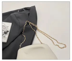 Close-up of cream acrylic clutch bag with gold chain strap on grey blazer fabric